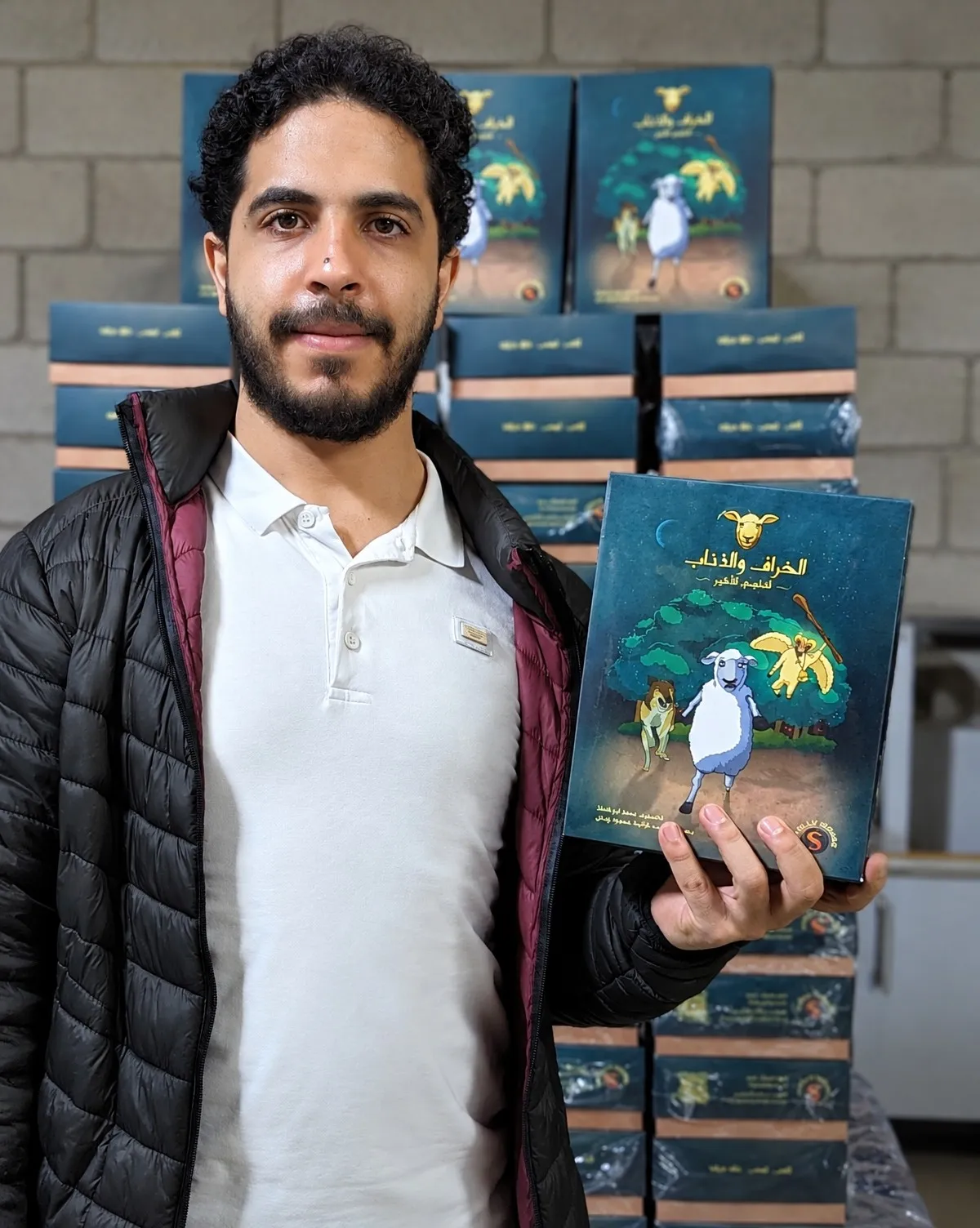 Mohamad holding a copy of Sheep & Wolves in front of stacked boxes from the first print run